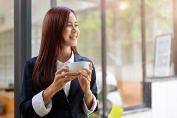 Relaxed and pleased asian businesswoman holding a coffee cup, sipping morning coffee