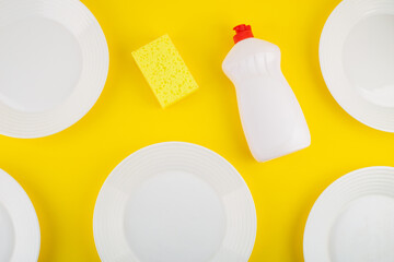 Cleaning yellow sponge and detergent for dishes on a yellow background with white plates. Top view, flatlay, close up. Concept cleaning company, purity, cleaning, kitchen