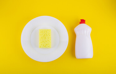 Cleaning yellow sponge on a white plate and detergent for dishes on a yellow background. Top view, flatlay, close up. Concept cleaning company, purity, cleaning, kitchen