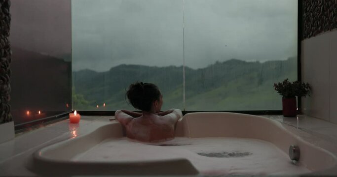 Beautiful woman alone in bubble bath looks out to mountain scenery - luxury