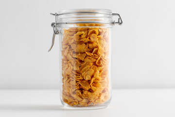 food, eating and storage concept - close up of jar with corn flakes on white background