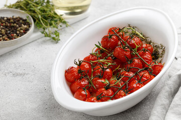 Baked mini cherry tomatoes with oil, garlic and thyme in white baked dish. Diet dinner idea. Vegetable, vegan.