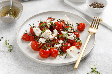 Baked cherry tomatoes and Feta cheese with oil, garlic and thyme in white plate. Diet dinner salad idea.