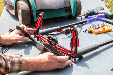 A man is repairing a battery-powered lawnmower. The electric toggle switch to start the engine is defective and needs to be replaced. A craftsman at work.