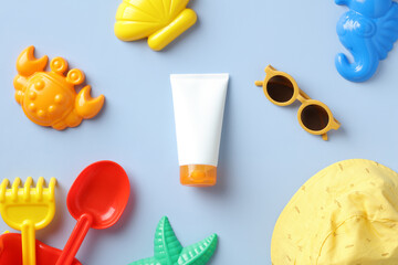 Sunscreen lotion tube with baby accessories on blue table. Flat lay, top view.