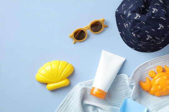 Sunscreen cream tube with baby sunglasses, sand molds, panama hat on blue table.