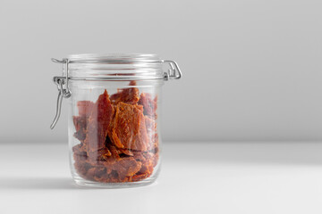 food, eating and storage concept - jar with beef jerky or pastrami on white table