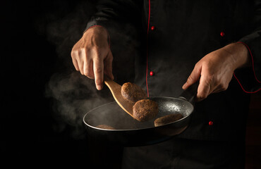 Meat steaks on barbecue grill on wooden tool. Cooking cutlets from beef or pork in a pan in the hands of a chef. Space for hotel menu on black background