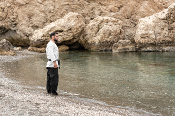 Martial arts master in kimono with black belt with his feet in the water at the shore of the beach...