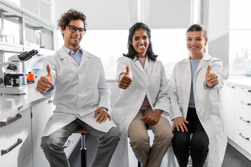 Fototapeta na wymiar science, work and people concept - international group of happy scientists showing thumbs up in laboratory