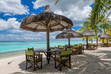 Beach cafe on sandy beach under straw umbrella, palm trees and beautiful sea on exotic tropical island.	