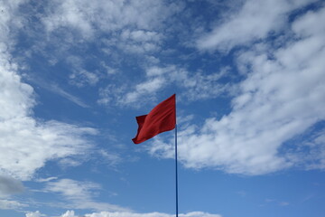 red flag on a blue cloudy sky in summer prohibit swimming