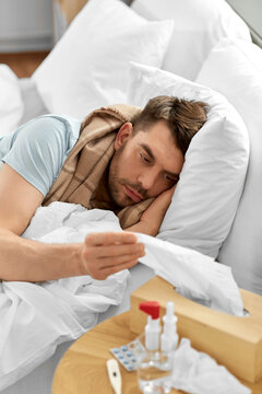 people and health problem concept - unhappy sick man lying in bed at home and taking paper tissue from box