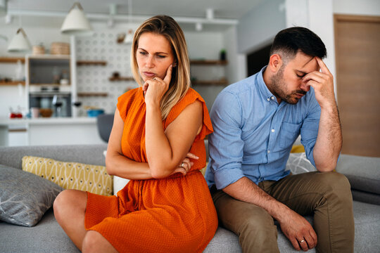 Sad pensive couple thinking of relationships problems sitting on sofa, conflicts in marriage.