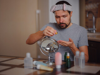 Men's beauty concept. caucAsian guy checking his skin. Skin nutrition. Young man applying organic essential serum on face with pipette, free space - obrazy, fototapety, plakaty