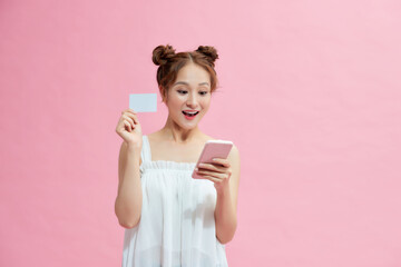 Portrait of a smiling woman holding credit card and mobile phone over pink background