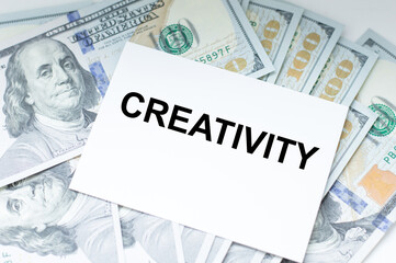 Naklejka premium Creativity text on a card against the background of dollar bills on the table