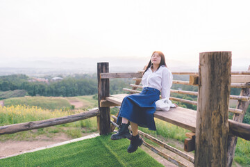 Fototapeta premium Asian woman wearing white twisted shirt siting on a bench in the morning of refreshing atmosphere.