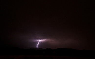 Au loin, des millions de watts,lightning emerging from a layer of black clouds in the night