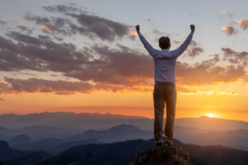 Fototapeta na wymiar Success concept.Male business standing on top rock with his hands raised enjoy sunny day