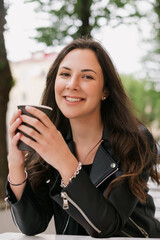A young woman drinks coffee from a paper cup outside