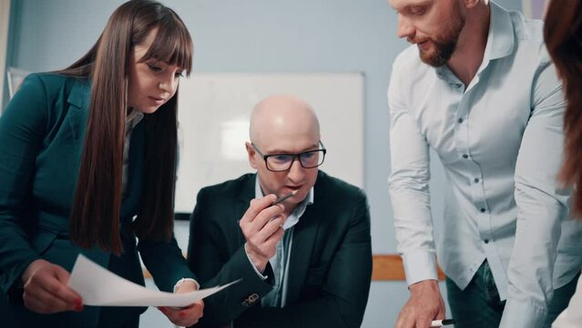 The boss is discussing a project with his subordinates in the office. A team of young business people at a conference. Zoom out.