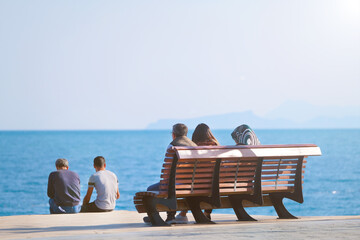 People of various religion rest and sit side by side on a bench against the backdrop of the sea in a city park