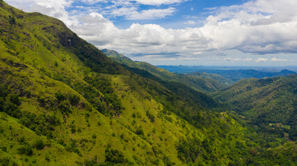Aerial view of Mountains covered rainforest, trees and blue sky with clouds. Ella Rock, Sri Lanka.
