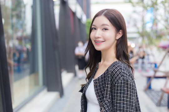 Portrait of a beautiful, long-haired Asian female in a black pattern coat with braces on teeth walking and smiling outdoors in the city.
