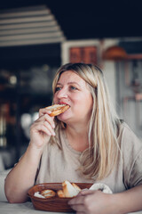 Woman tastefully bites off the slice of bread. Appetizing eating. Charming blond plus size woman eating fresh toasted bread in restaurant