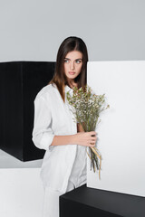 brunette woman with bouquet of gypsophila flowers near black and white cubes isolated on grey.