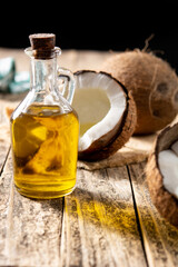 sliced coconuts with oil inside and bottle of coconut oil on wooden table	