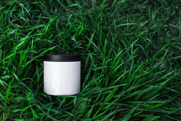 One white plastic jar on green grass background. Cosmetic packaging, blank mock up bottle. Beauty, skin care, natural organic eco body treatment concept. Flat lay, top view, place for text. Like 3d