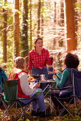 Group Of Female Friends On Camping Holiday In Forest Drinking Coffee Sitting By Tent Together