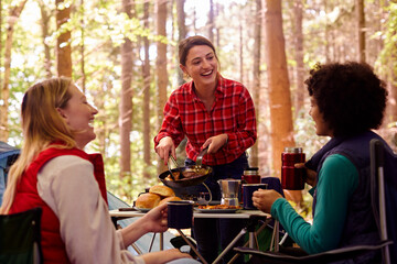 Group Of Female Friends On Camping Holiday In Forest Eating Meal Sitting By Tent Together