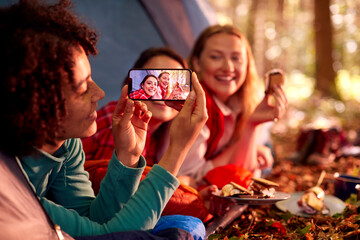 Woman Taking Photo Of Friends On Camping Holiday In Forest Lying In Tent Eating S'mores