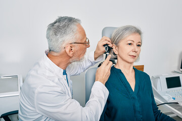 Otolaryngologist doctor checking senior woman's ear using otoscope or auriscope at hearing center....
