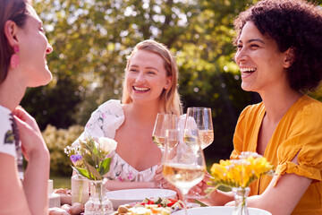 Three Female Friends Sitting Outdoors In Summer Garden At Home Eating Meal Together