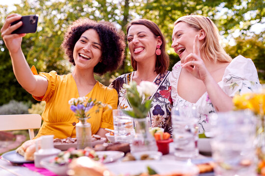 Three Female Friends Taking Selfie On Mobile Phone Eating Meal Outdoors In Summer Garden At Home