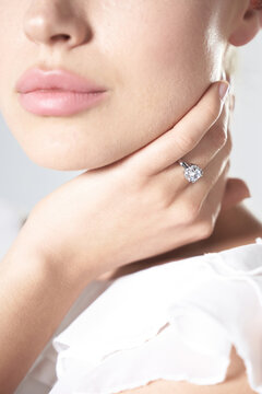 Cropped shot of a lady wearing a metal silver ring with a large clear sparkling crystal. The girl is dressed in a white blouse. The photo is made on the light background.