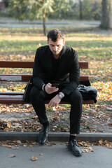 Obraz premium A young businessman is sitting on a park bench using a smartphone