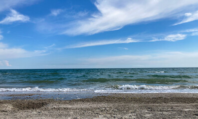 Sea beach with a beautiful and clean sea. The shore with wet sand. In the background is a vast, blue sky with some white and fluffy clouds.