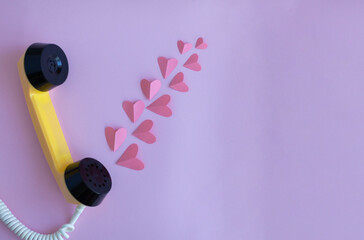The handset of a yellow retro phone on a pink background. Pink hearts come out of the handset of the phone. The concept of love calls and Valentine's Day. Banner with space for text