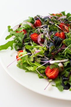 Light salad with arugula and berries, strawberries and blueberries, delicious healthy summer salad on a white background