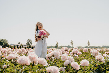 Fototapeta na wymiar Young sexy beautiful girl collects flowers on a pink peony field. Woman on vacation roaming the flower garden. Leisure concept. Basket with flowers