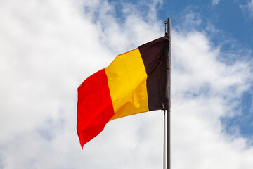 The flag of Belgium flutters in the wind against a cloudy sky