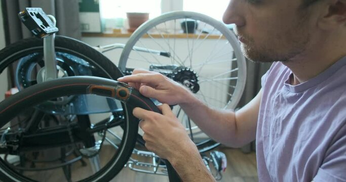 man inspects bicycle inner tube for punctures. Trying on a tire. Looks at the sealed patches. The concept of a home bike workshop, do it yourself, repair it. Close-up, indoors.