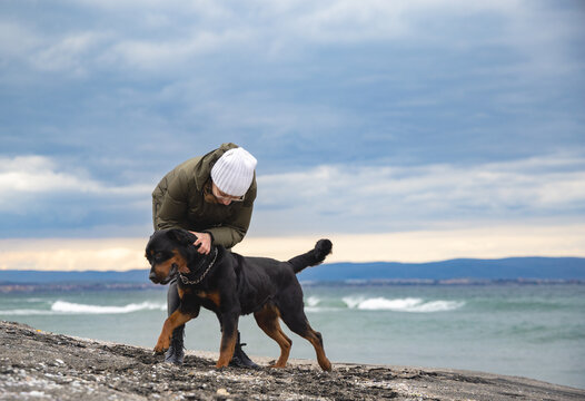 Woman fooling around with rottweiler dog in cold weather on the beach