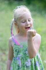 Fototapeta premium A little girl looks at a butterfly on her hand in the summer meadow