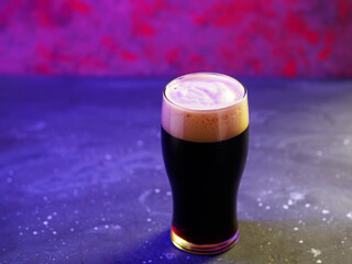 A glass of dark craft beer , porter or stout on a purple neon background